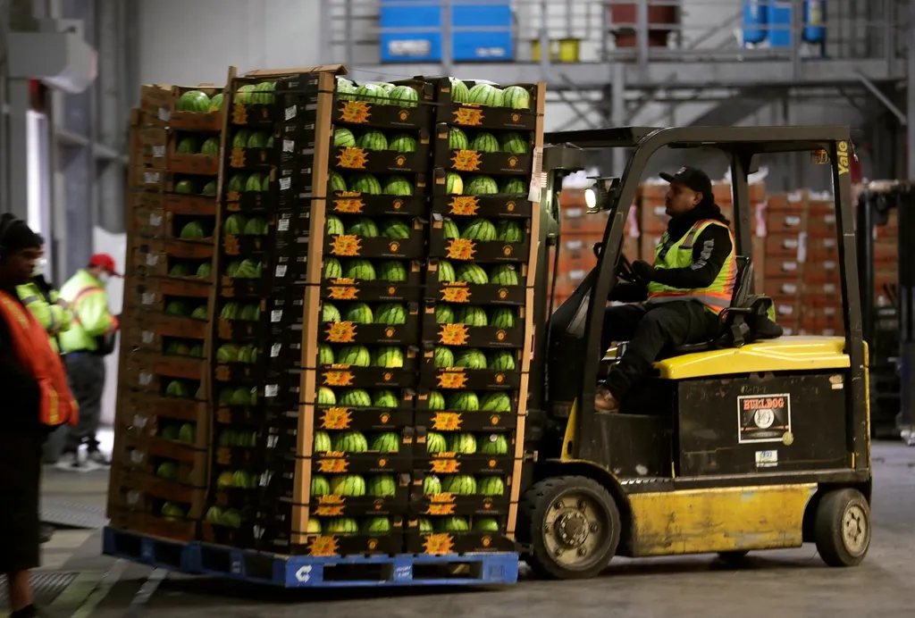 Forklift moving a tall pallet of produce crates at a loading dock, with workers nearby and detected objects boxed